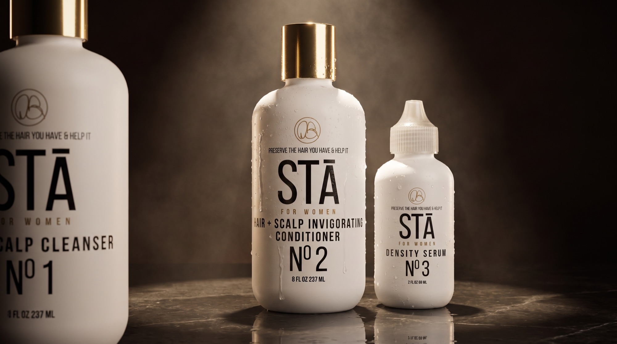 The STĀ For Women system under studio spotlight: Scalp Cleanser Nº1, Hair + Scalp Invigorating Conditioner Nº2 and Density Serum Nº3, beaded with water droplets
